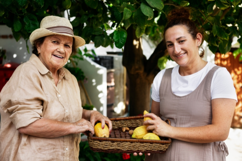 Una mujer anciana practica turismo slow en un mercado de proximidad. Sujeta una cesta de limones.